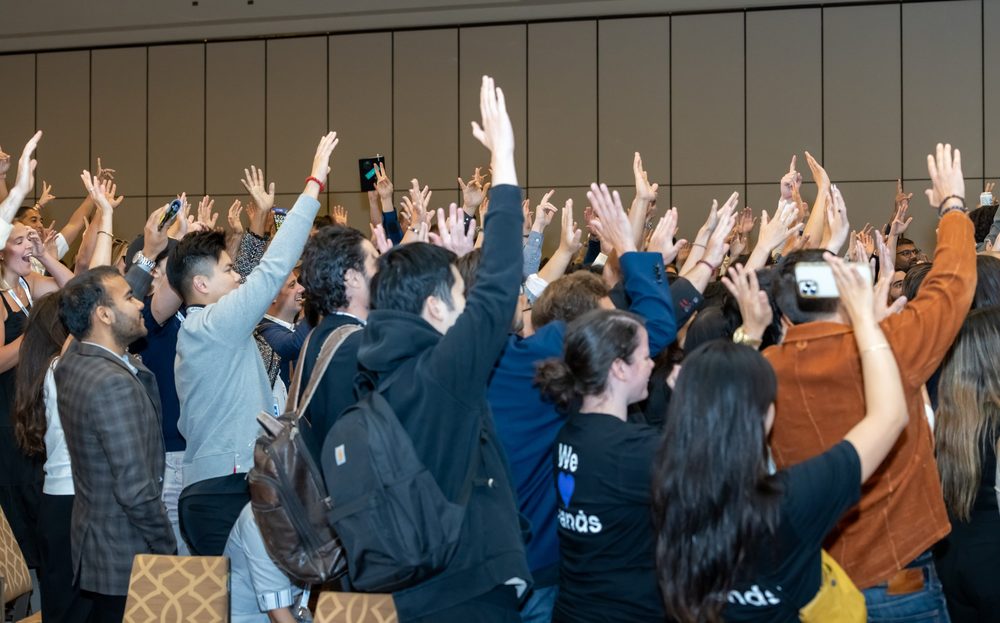 A crowd of attendees with their hands raised in the main room